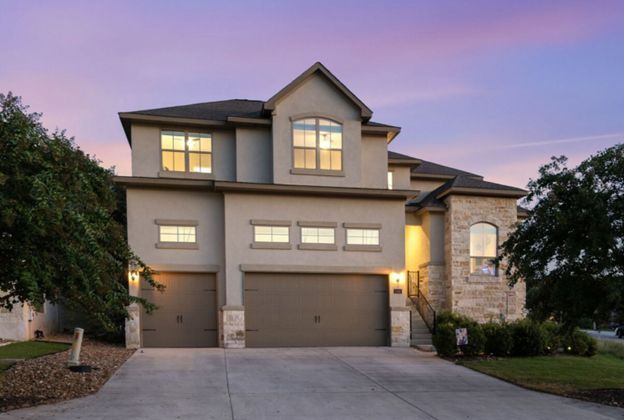 Two-story suburban house with lit windows, garage, and driveway at dusk