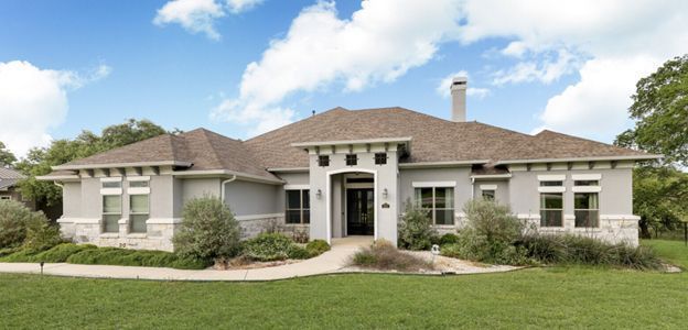 Single-story beige house with brown roof, white columns, and a manicured lawn under a blue sky