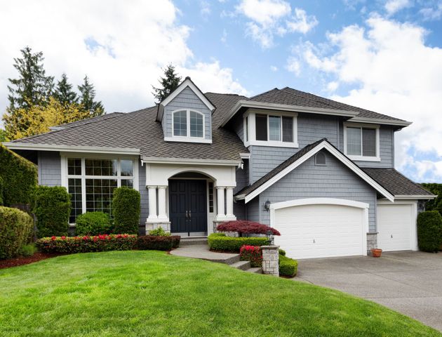 Gray two-story suburban house with a green lawn, white trim, and a two-car garage