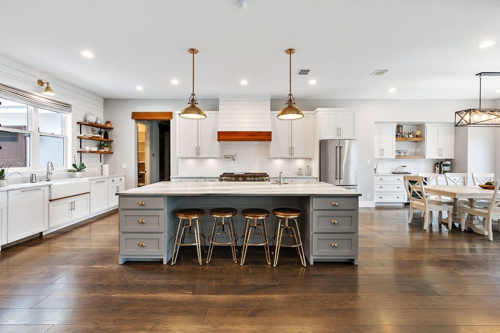 Bright white kitchen with a large island, pendant lights, bar stools, and dark wood floors