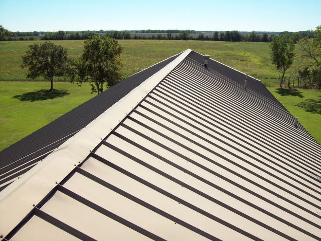 Metal roof on a sunny day with green trees and fields in the background.