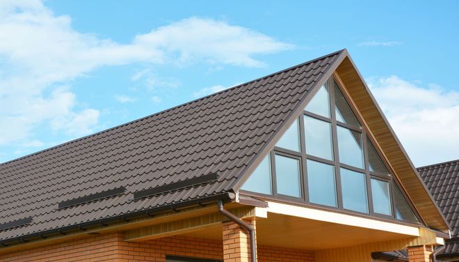Brown metal roof on a house with large triangular windows and a blue sky background.