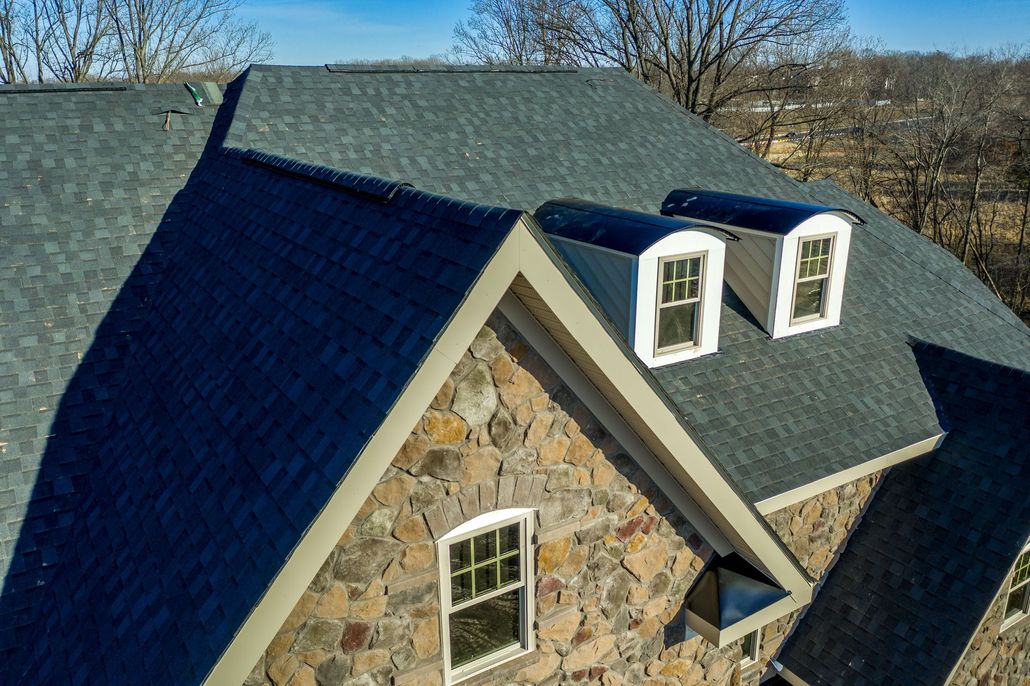 Stone house with a dark gray shingle roof and two dormer windows.