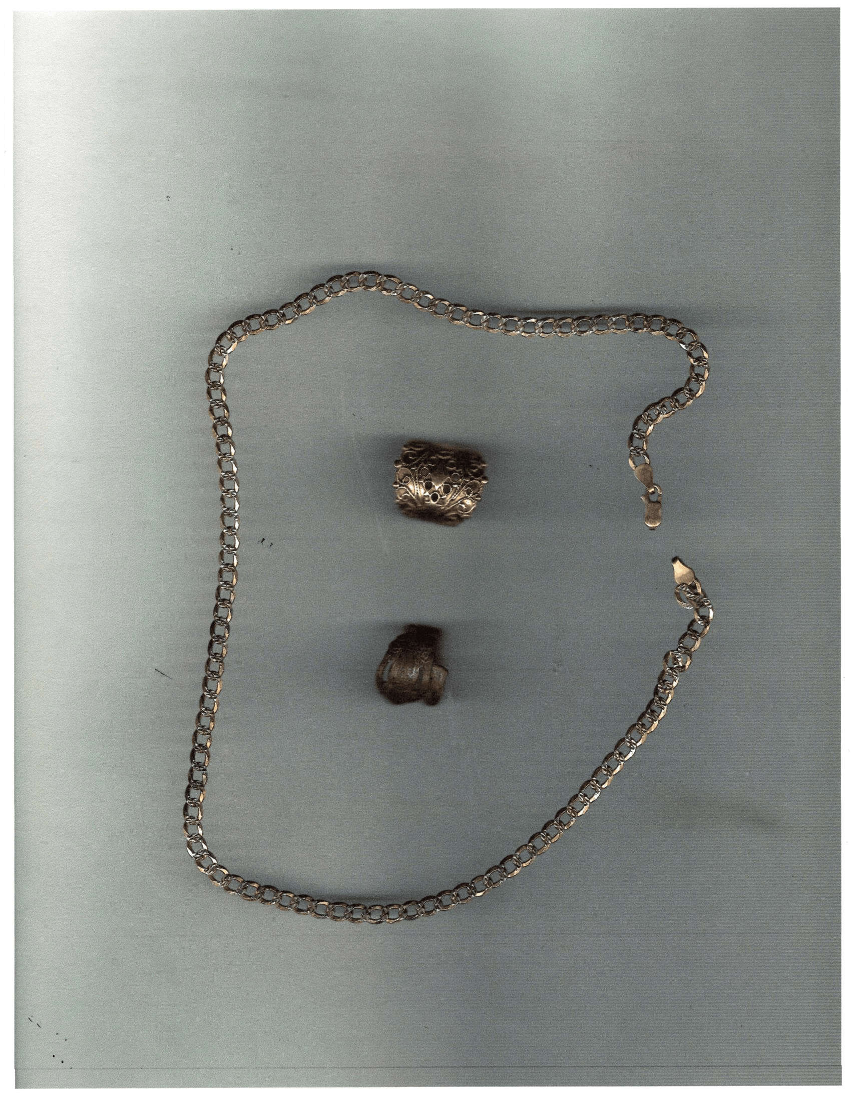 Small necklace chain arranged in an outline, with two dark beads on a gray background