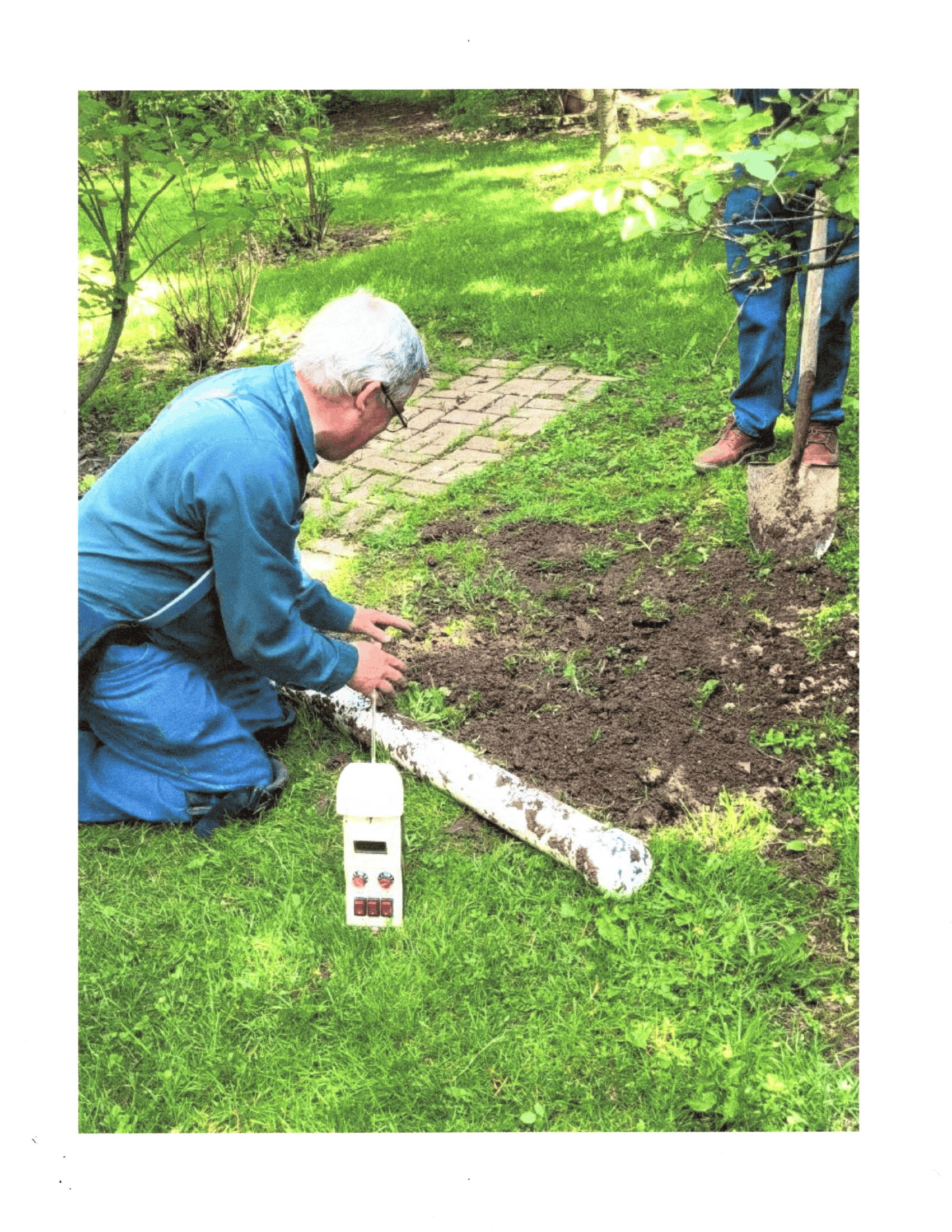 Person kneels in a garden, cutting a fallen tree branch beside a stone path.