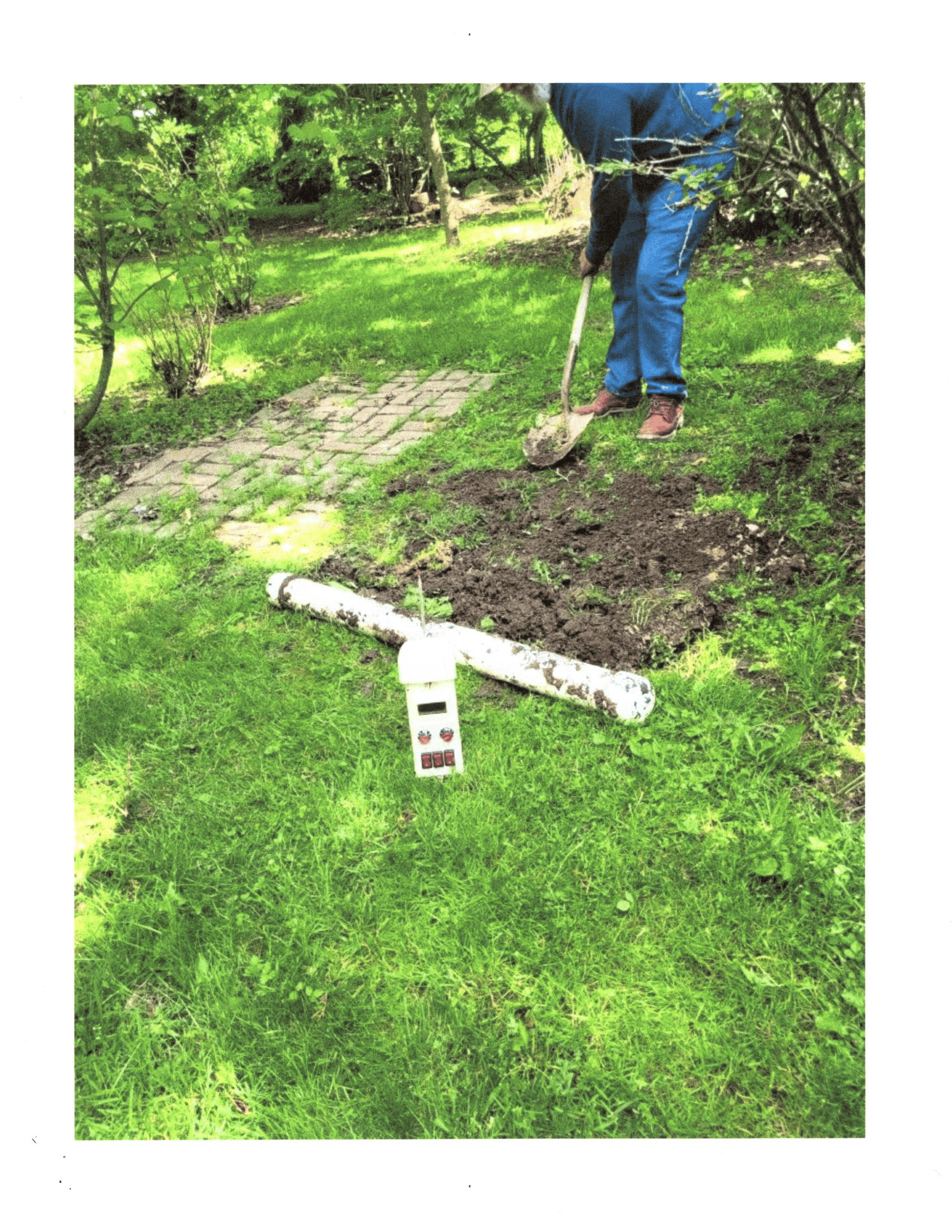 Person digging a garden bed in a green yard with a hose and shovel