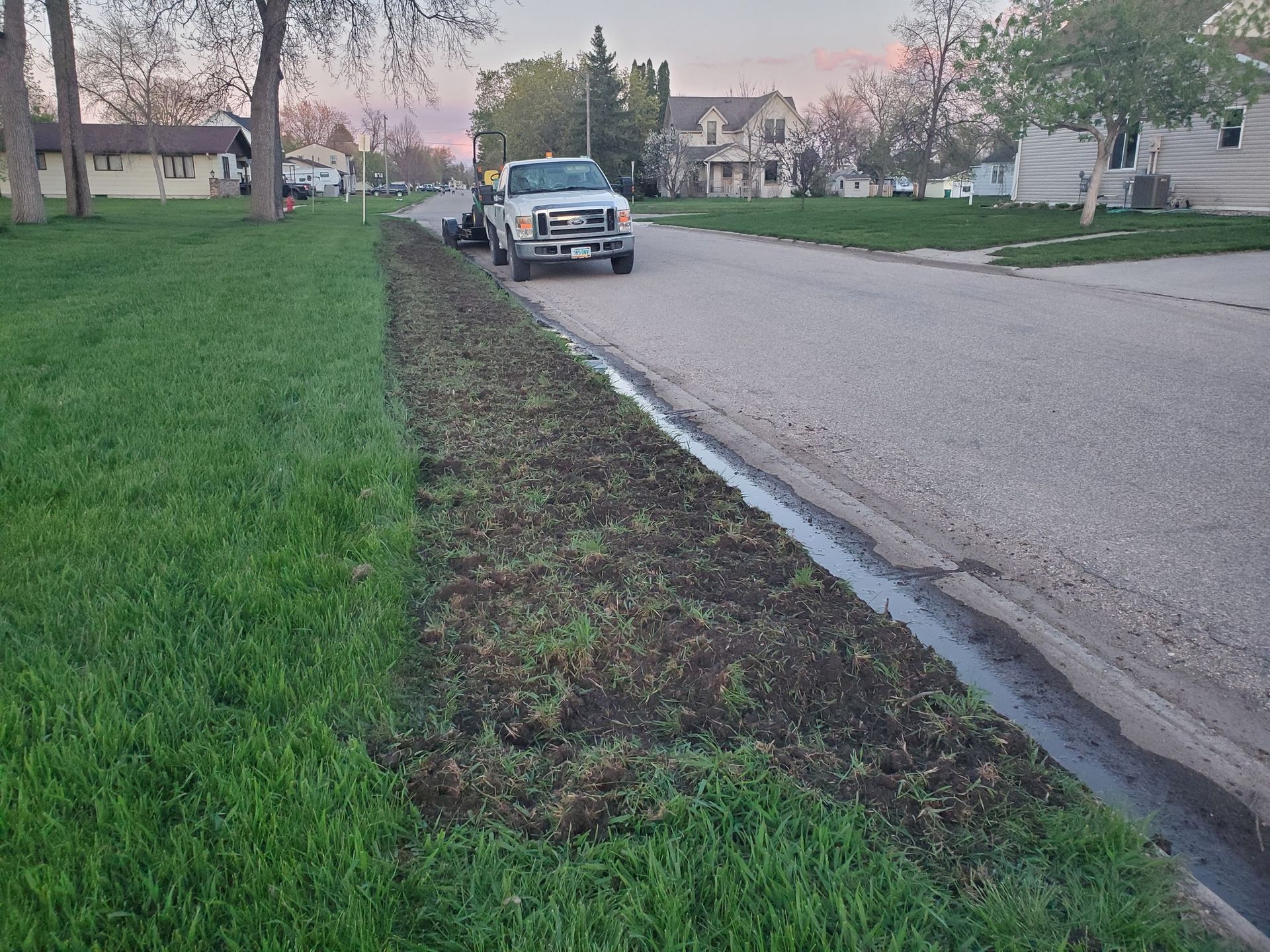 A white truck is parked on the side of the road next to a drain.