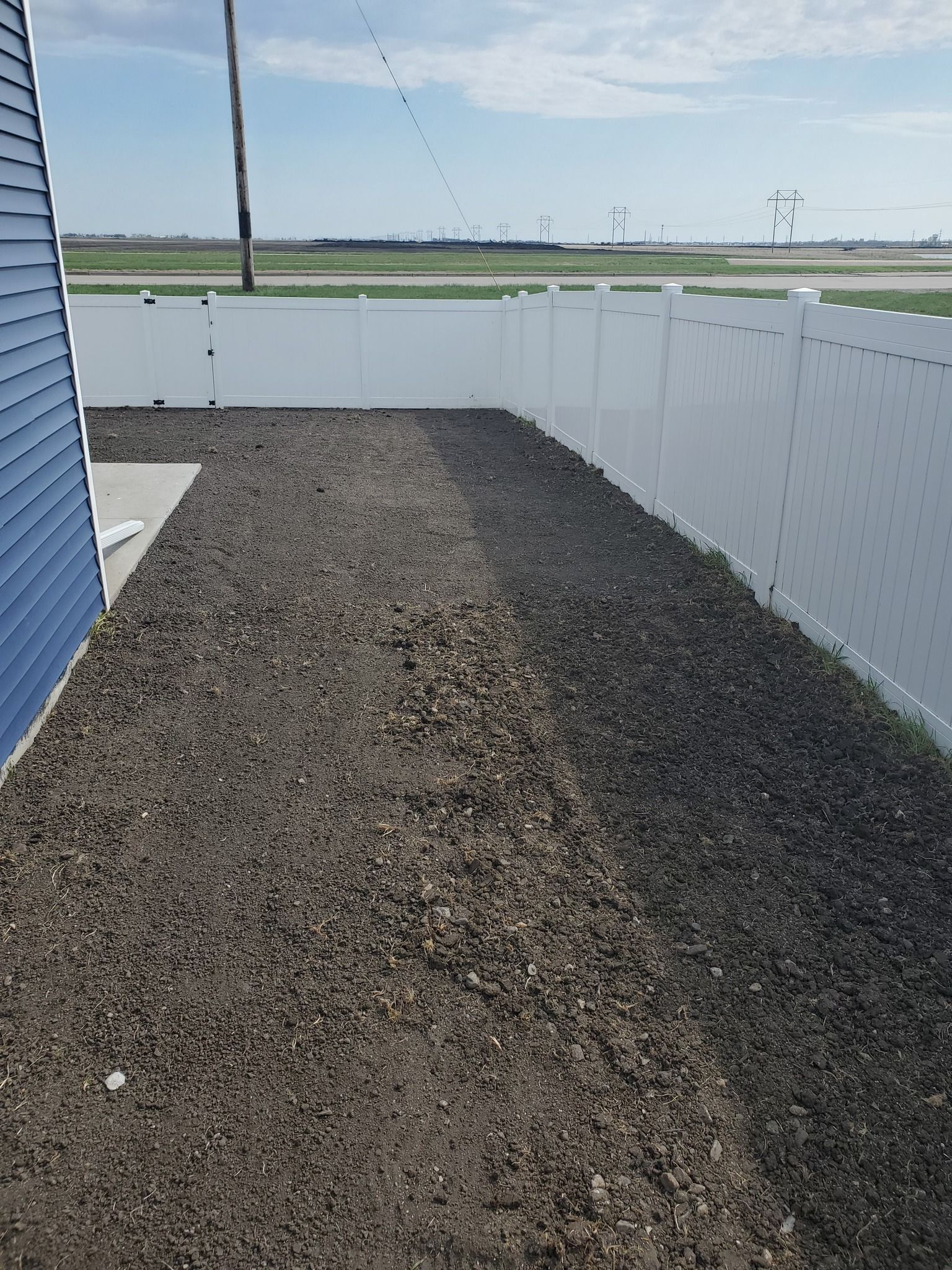 A white fence surrounds a dirt yard next to a house.
