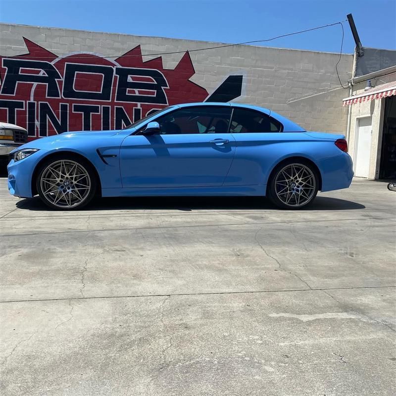 Blue BMW coupe parked in front of a tint shop mural on a sunny day