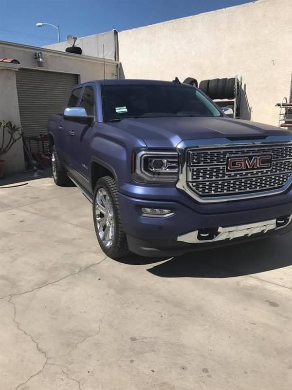 Blue GMC pickup truck parked in a sunlit driveway beside a beige building