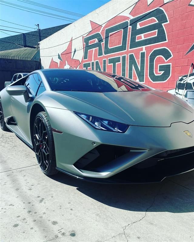 Matte green Lamborghini parked outside a wrap shop with a large mural backdrop