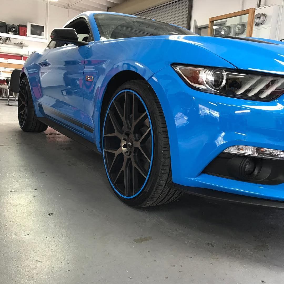 Blue sports coupe in a garage, low front-left angle, with black rims and a shiny finish