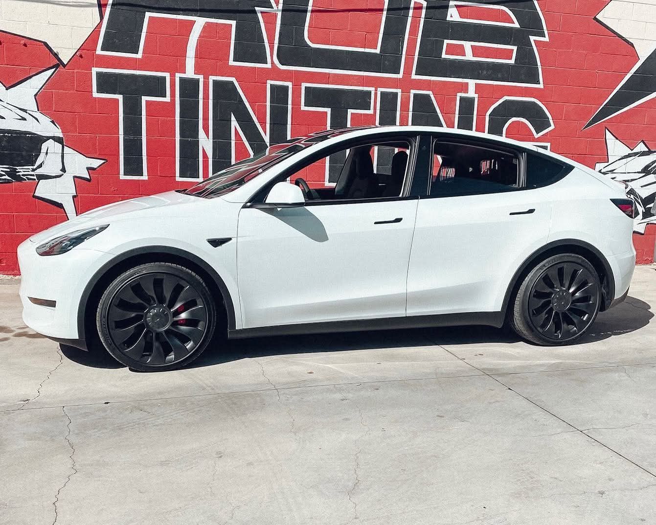 White Tesla SUV parked in front of a red wall mural reading “TRUE TINTING”