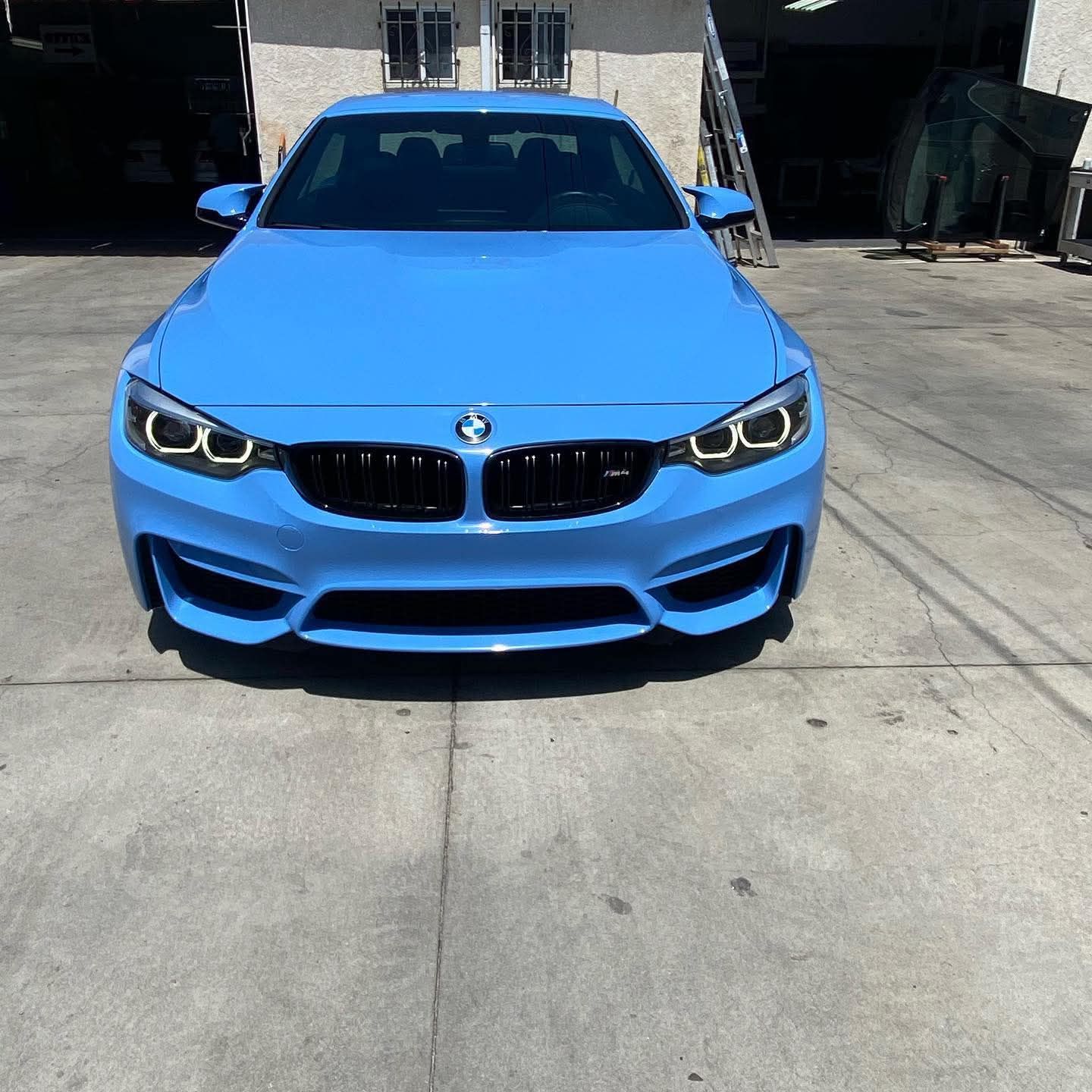 Bright blue BMW sedan parked on a concrete driveway, front view in direct sunlight.