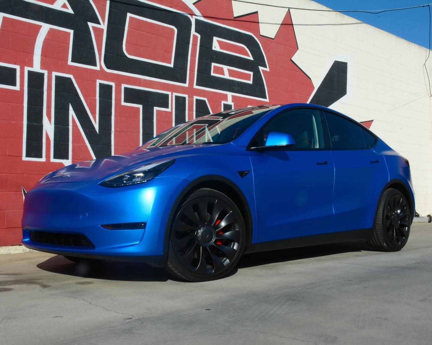 Blue Tesla sedan parked in front of a wall mural