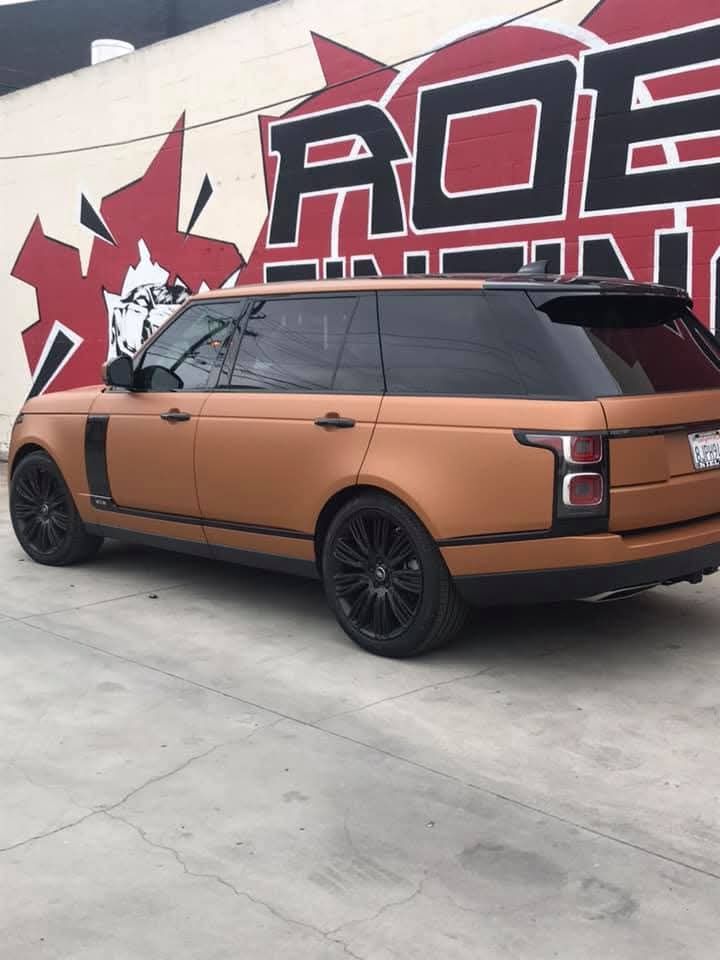 Bronze SUV with black wheels parked beside a mural wall outdoors.