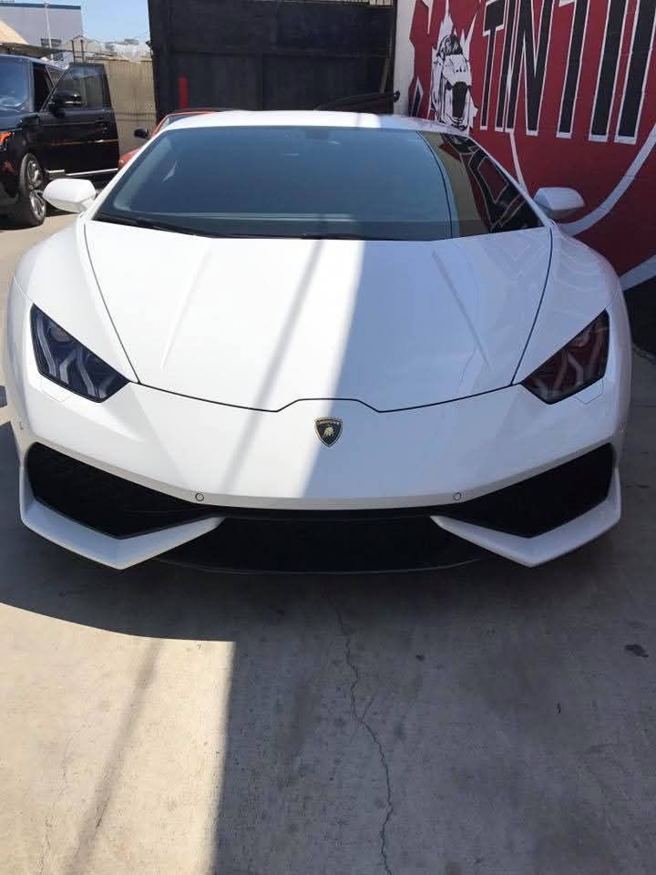 White Lamborghini sports car parked in a narrow alley, front view in bright sunlight.