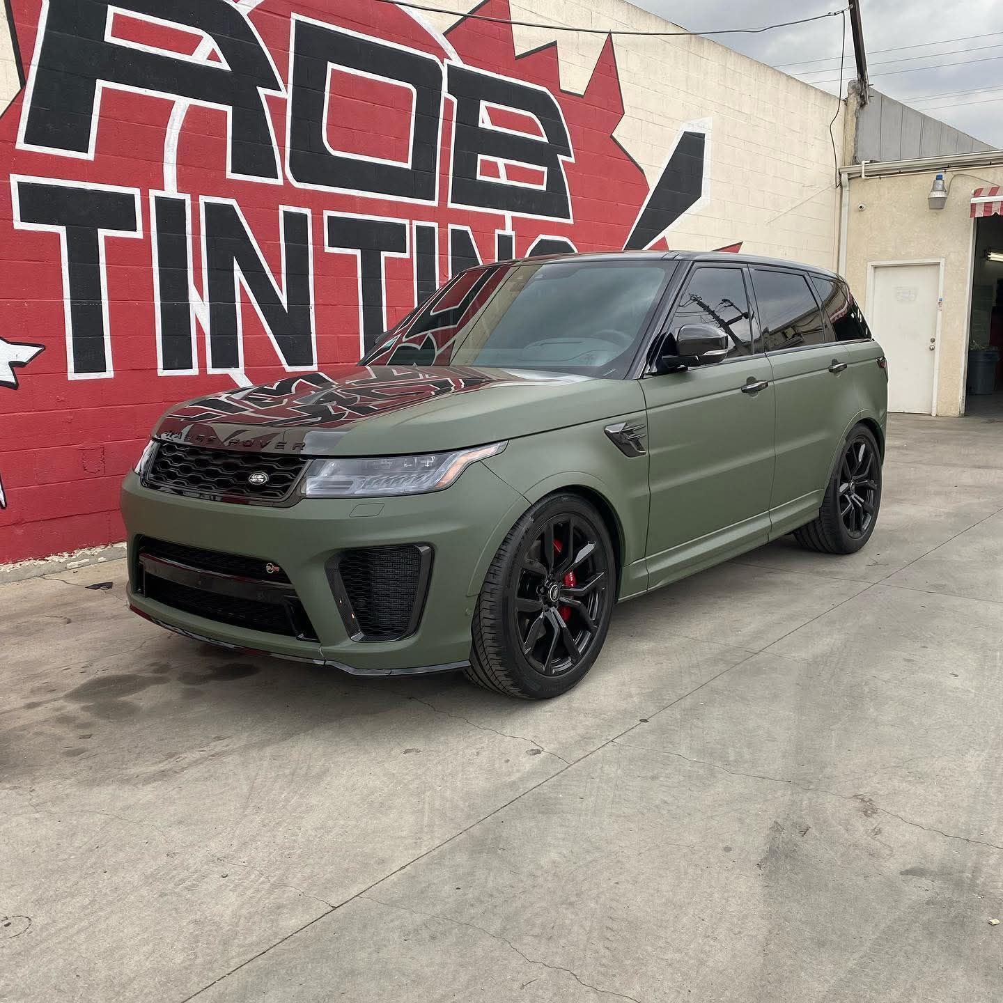 Matte olive green Range Rover parked outside a tint shop mural wall