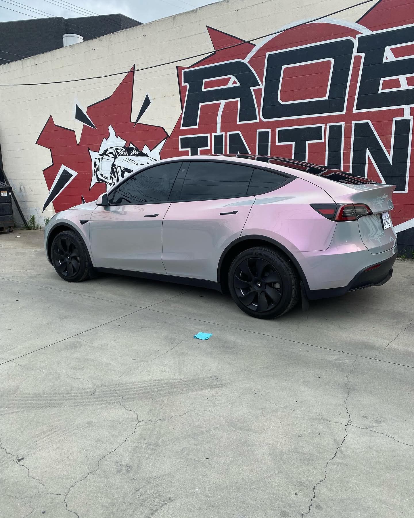 Pink Tesla SUV parked beside a mural wall with red and black lettering.