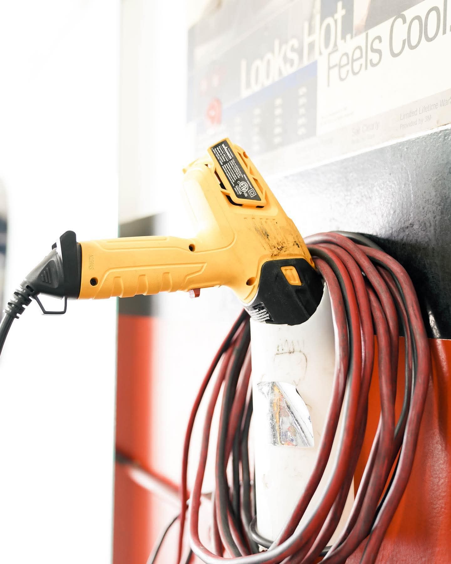 Yellow power drill hanging on a wall beside coiled red cable and a sign in a workshop setting