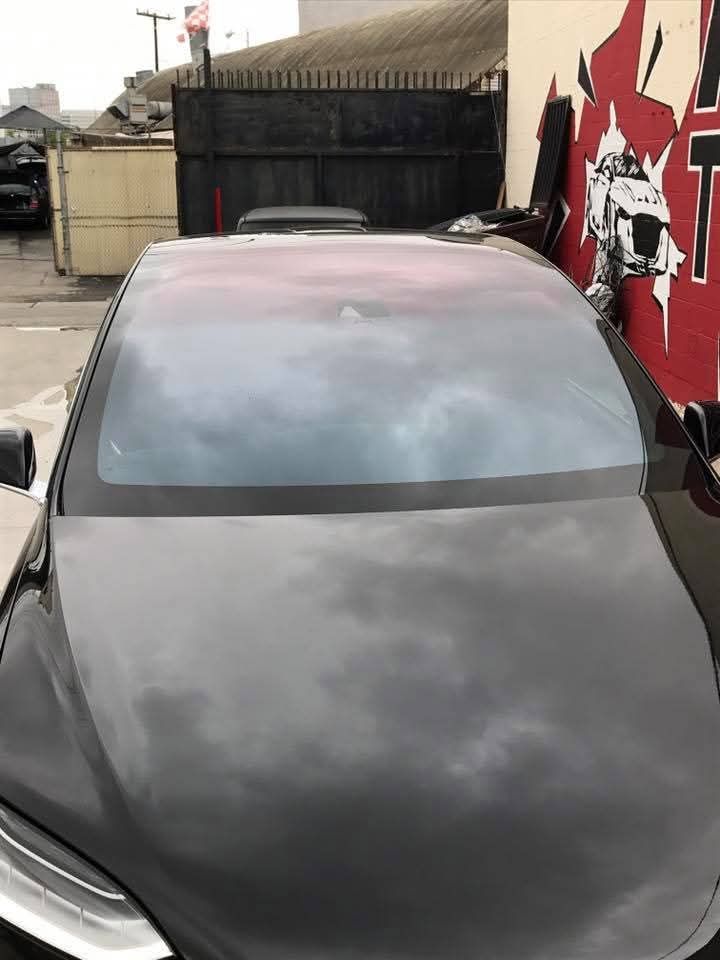 Black car parked in an alley beside a red graffiti wall and trash bins under cloudy reflections