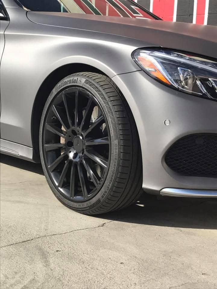 Silver car with black rims parked on a concrete surface, close-up of the front wheel and bumper