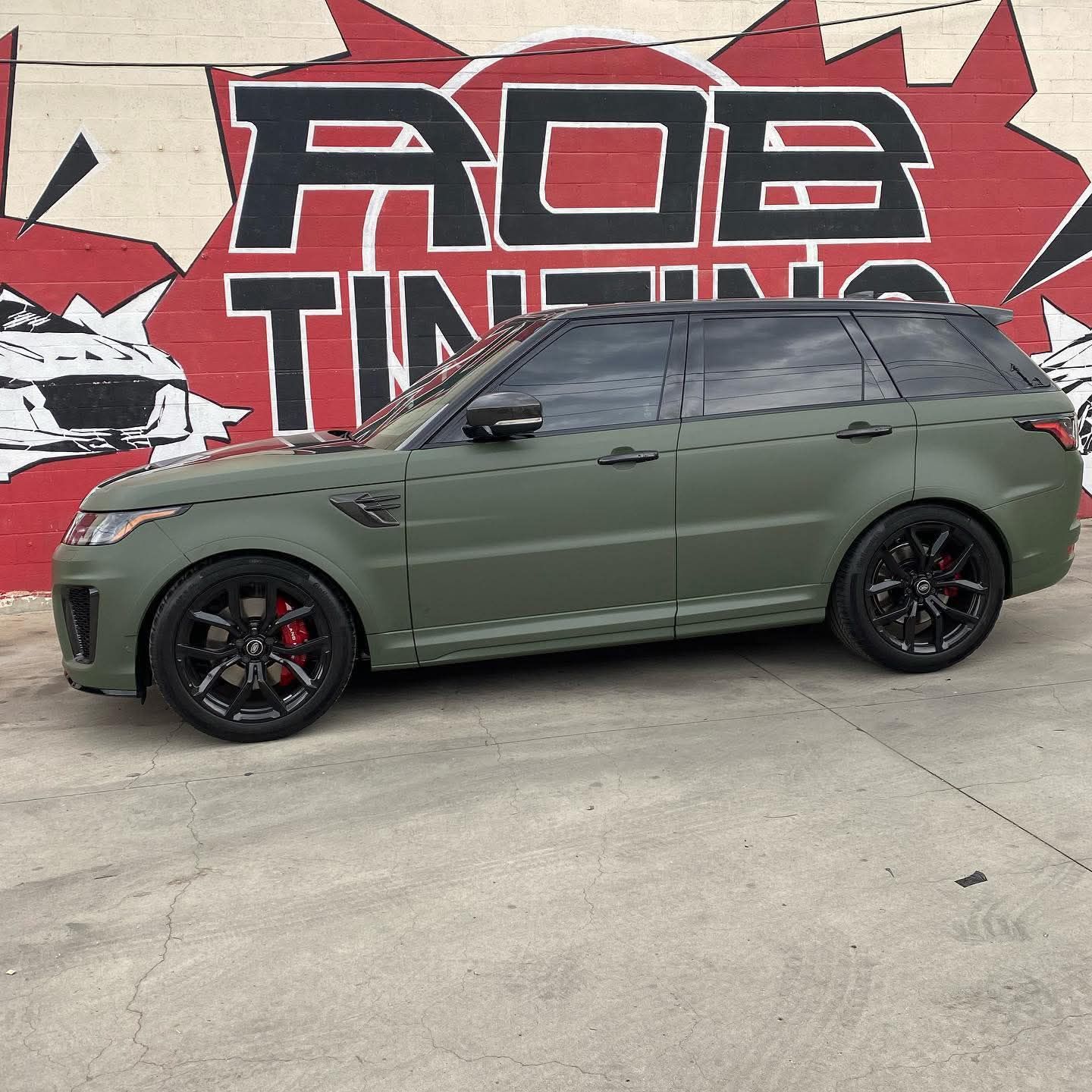 Olive green SUV with black wheels parked in front of a red and white mural