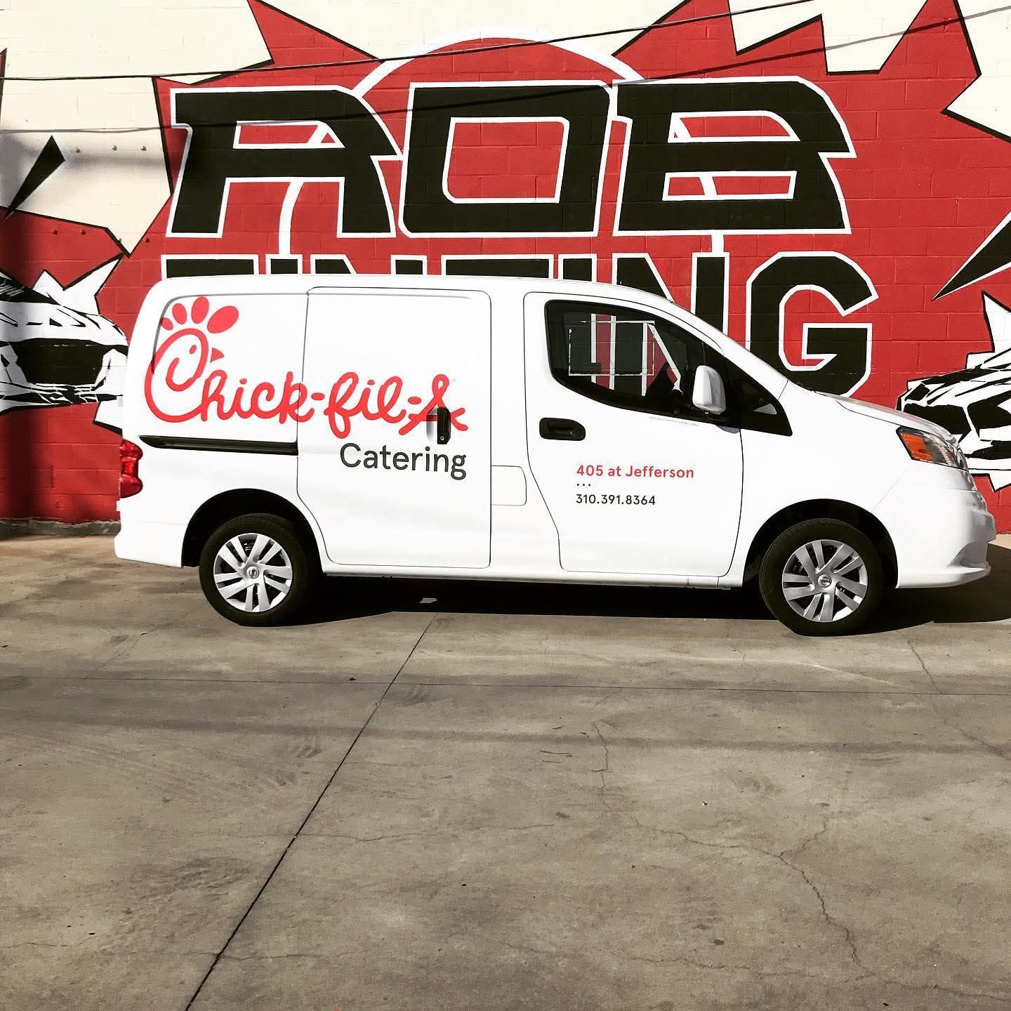 White Chick-fil-A Catering van parked in front of a red-and-black graffiti mural.