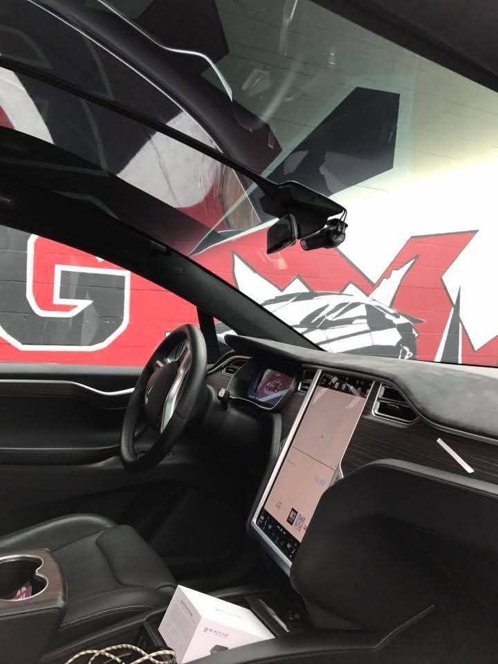 Inside a Tesla, showing the steering wheel, center screen, and a graffiti-style wall outside the window