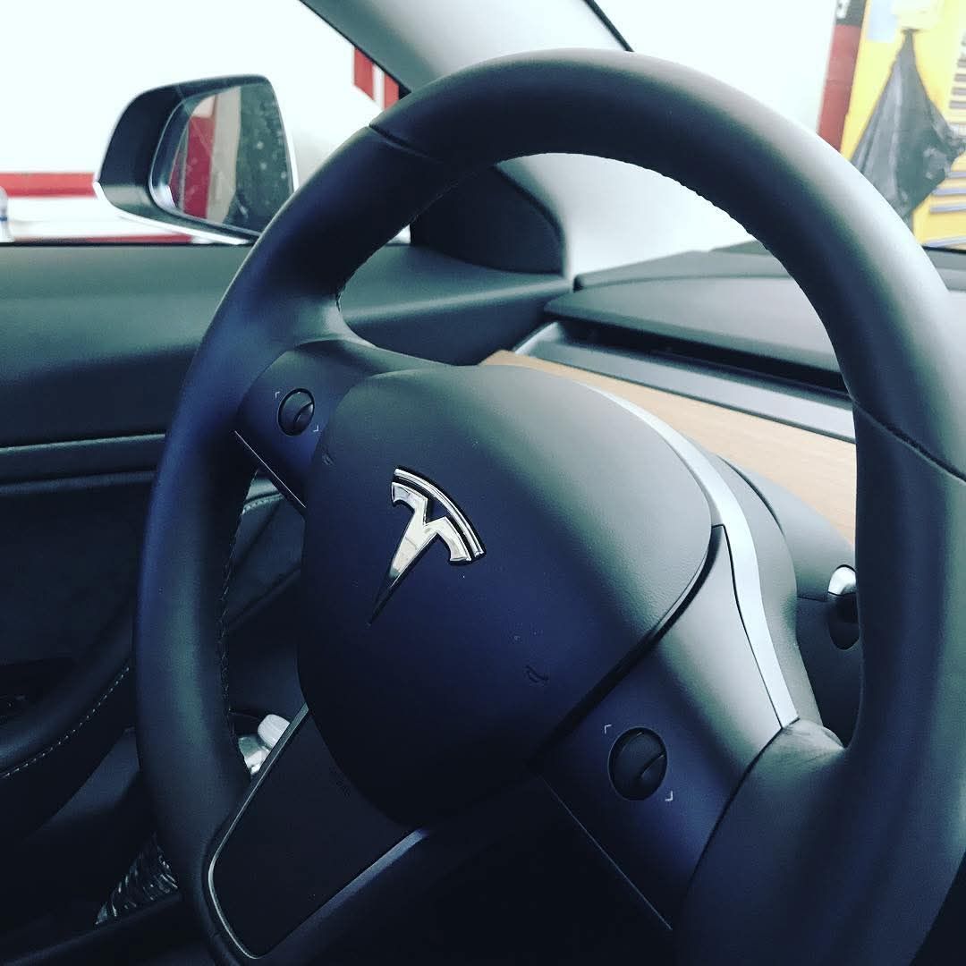 Tesla steering wheel and dashboard interior, with the Tesla logo centered on the wheel