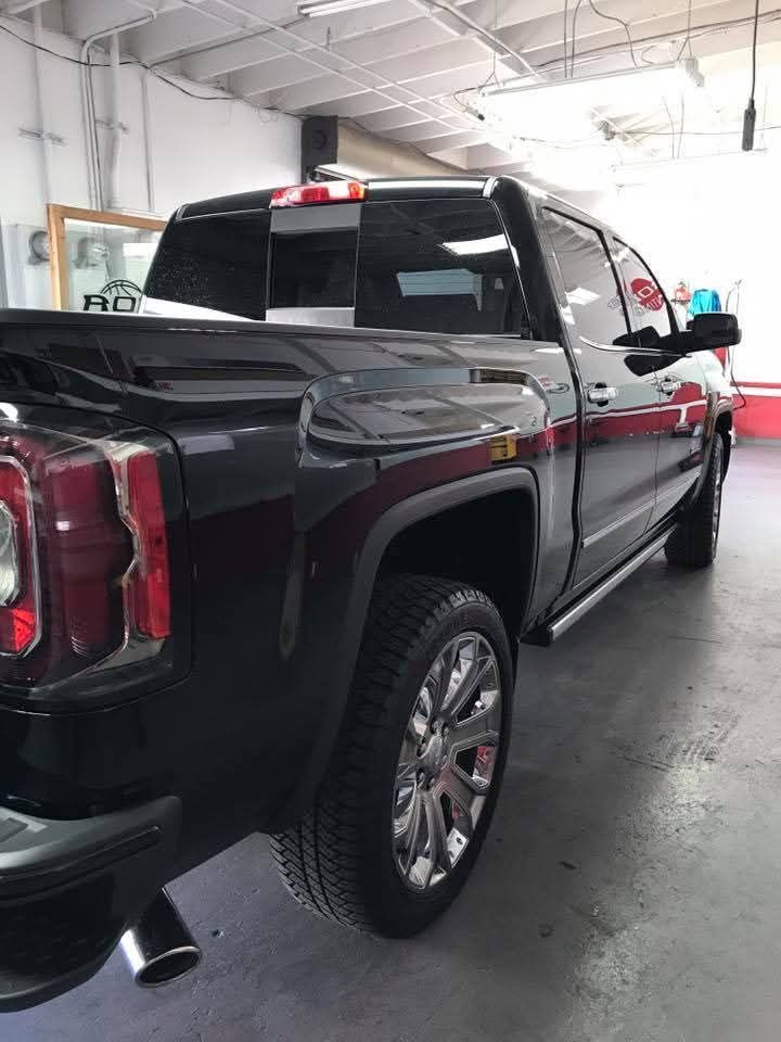 Black pickup truck parked indoors in a garage or service bay, rear three-quarter view