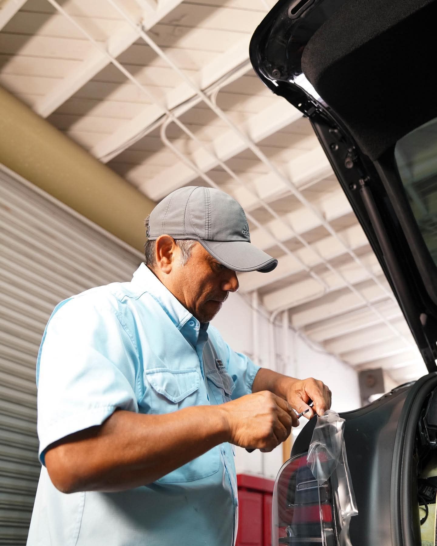 Mechanic in a gray cap working inside a vehicle garage beside an open car hood