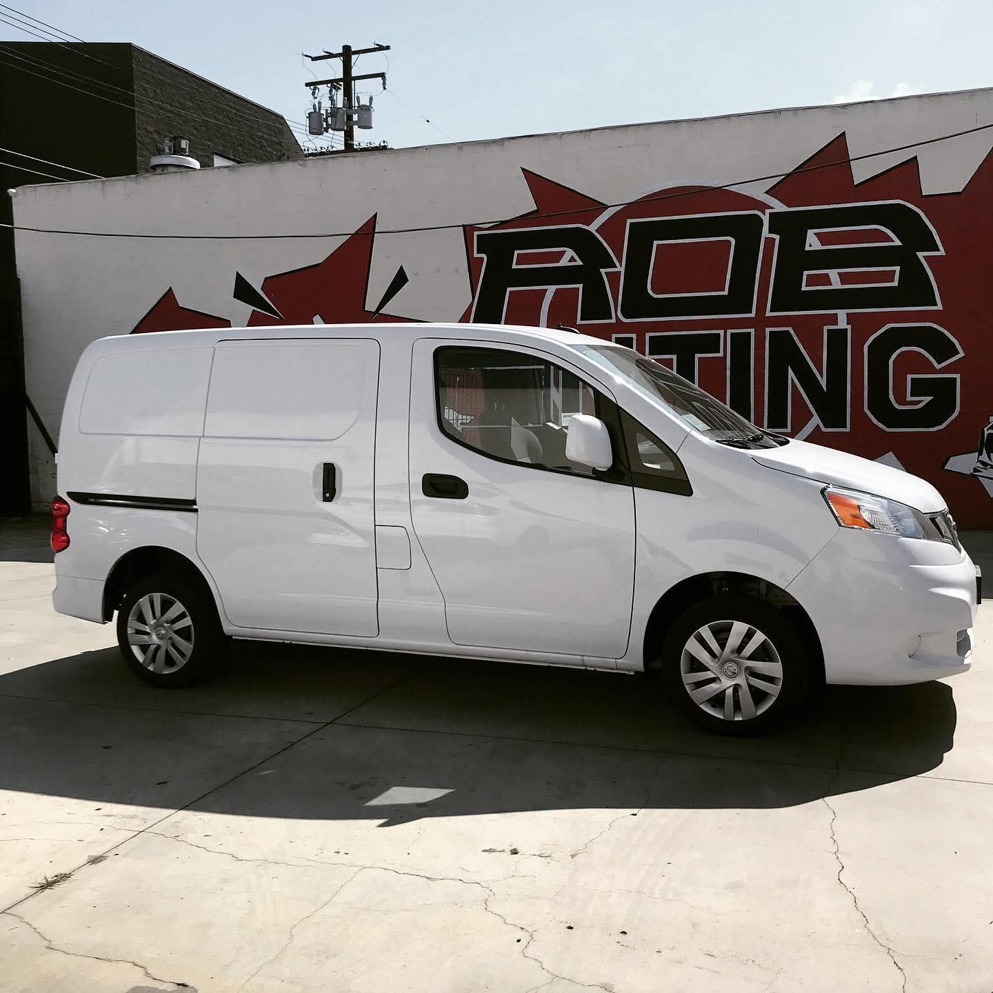 White cargo van parked beside a wall with a red-and-black graphic mural.