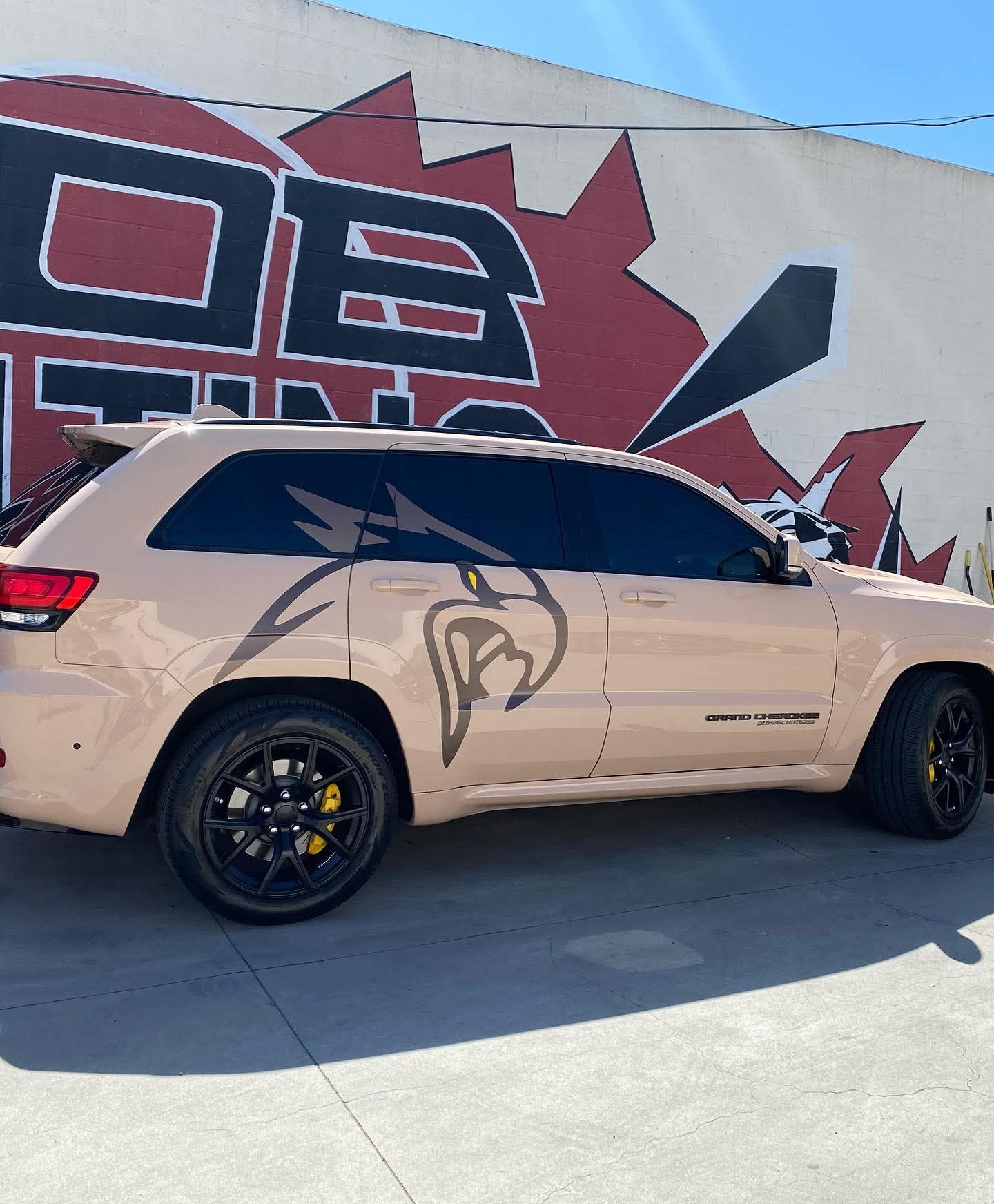 Beige SUV with black wheels parked beside a mural-covered wall.