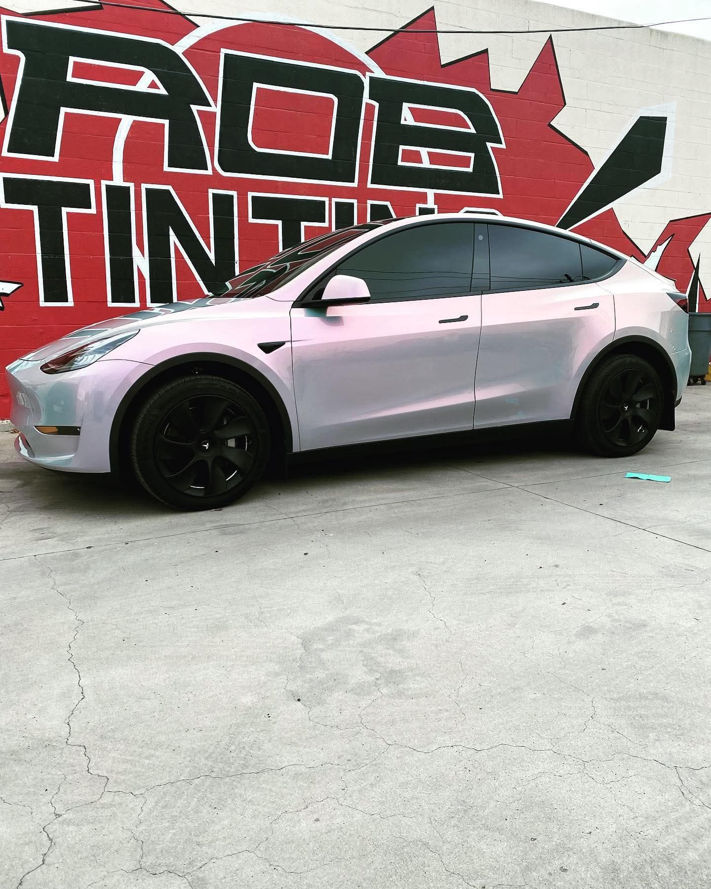 Silver Tesla Model Y with black wheels parked indoors in front of a graffiti wall.