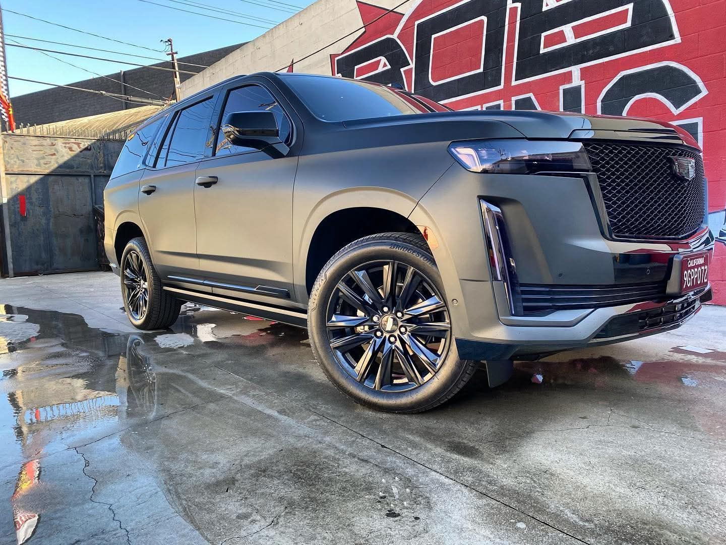 Black luxury SUV parked on a wet street beside a graffiti wall.