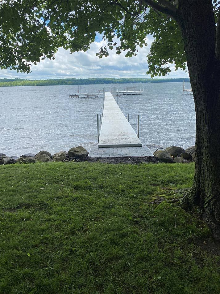 A dock leading into a lake with a tree in the foreground.