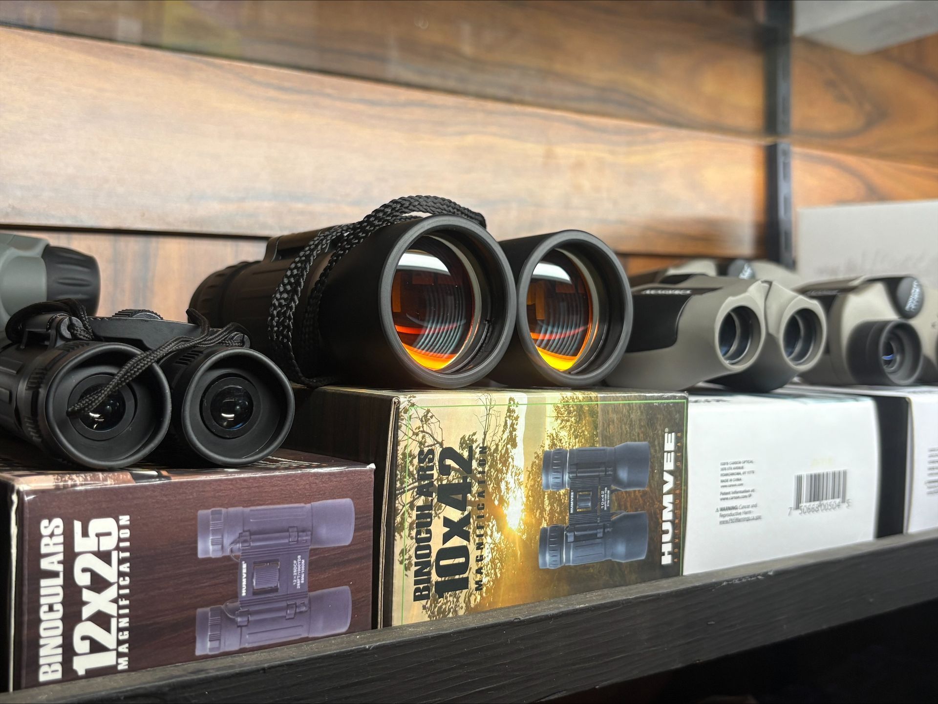Binoculars on a shelf with their boxes. Black, silver, and tan models. Wooden background.