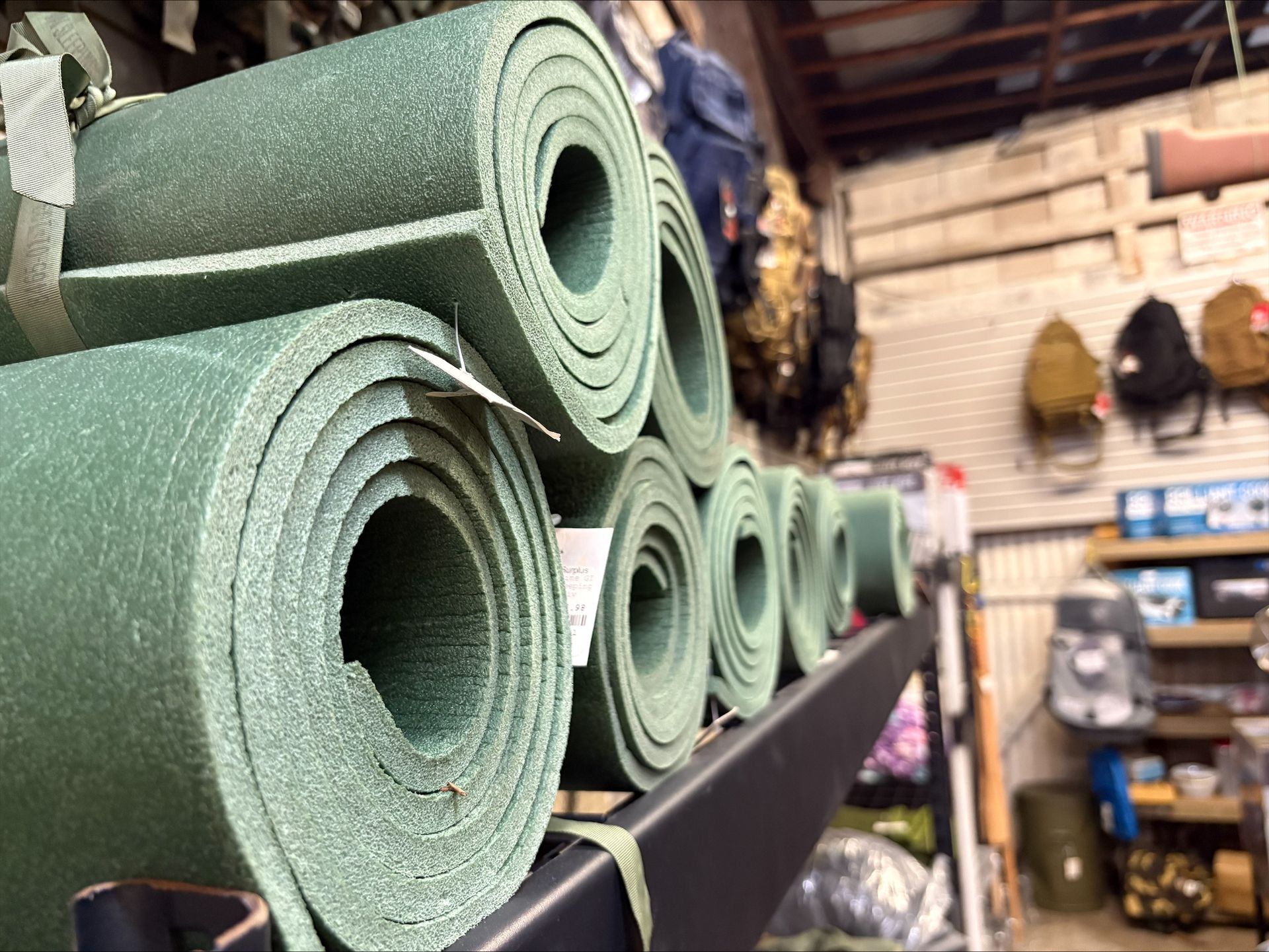 Green foam sleeping mats rolled up on a shelf inside a store.
