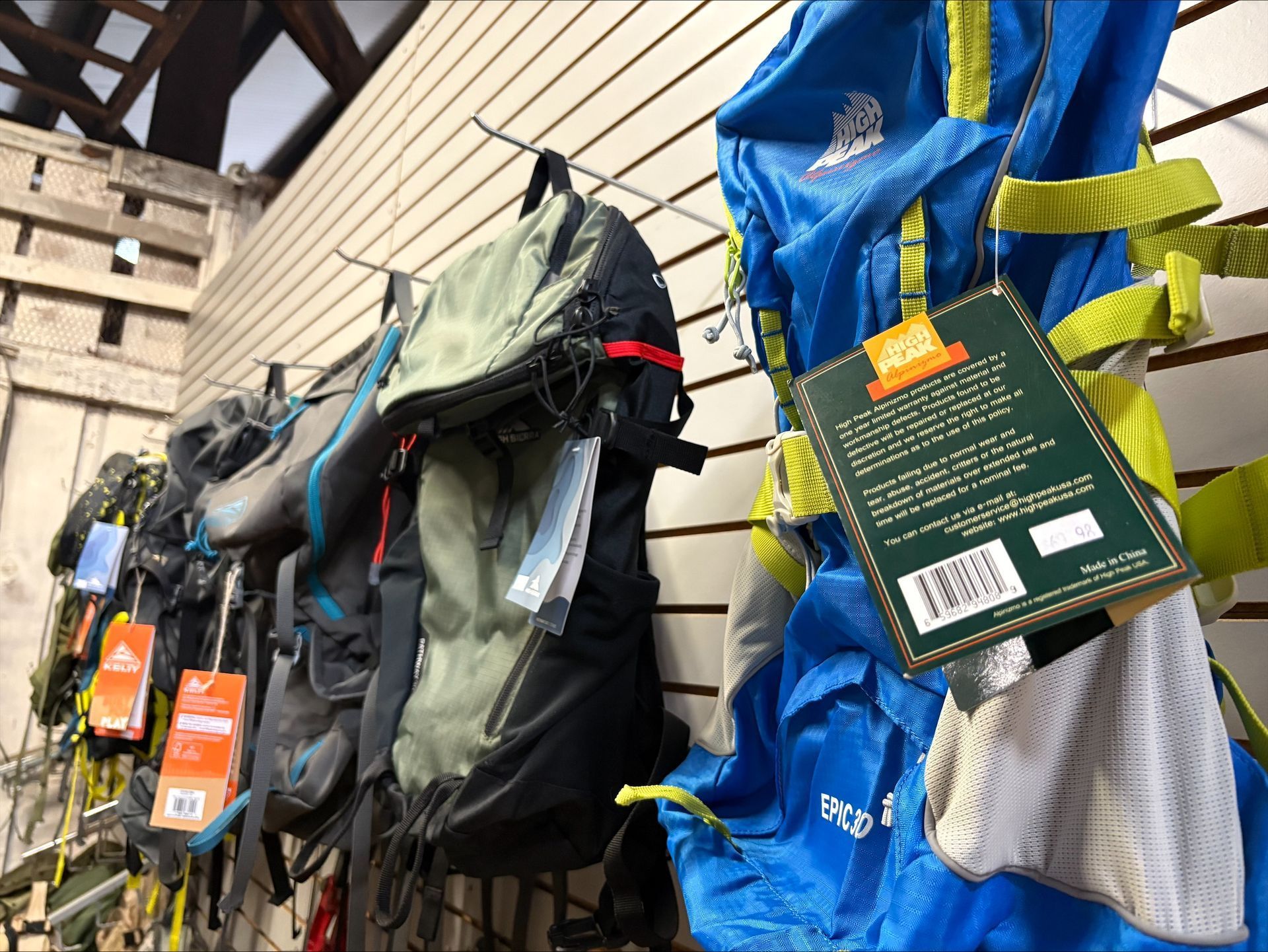 Backpacks hanging on a wall in a store, various colors, with price tags.