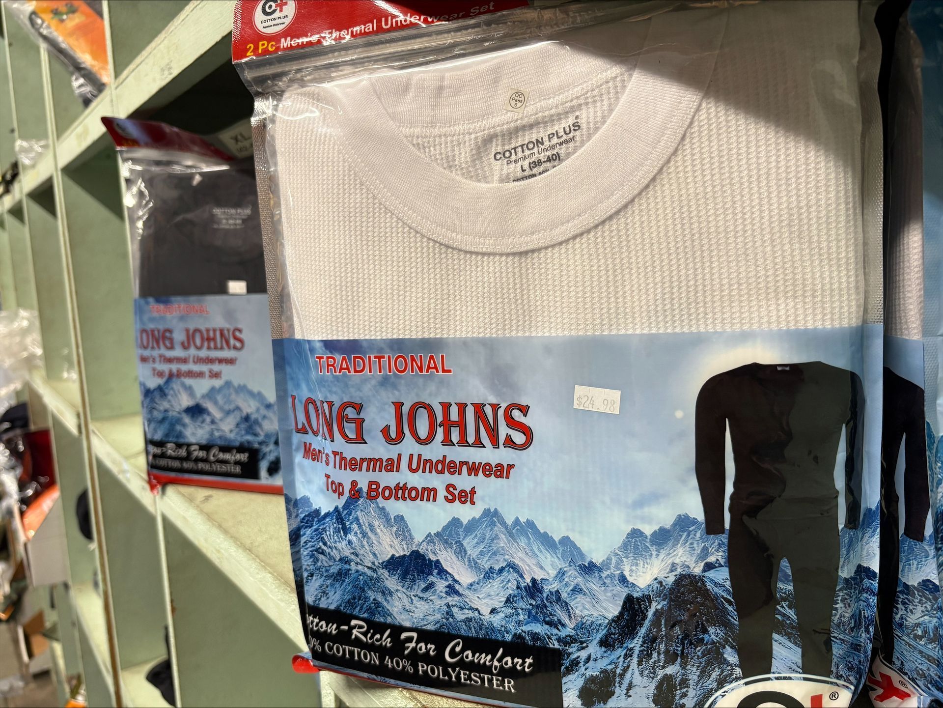Packages of thermal long john underwear on a shelf, white and black options, mountain graphic on packaging.