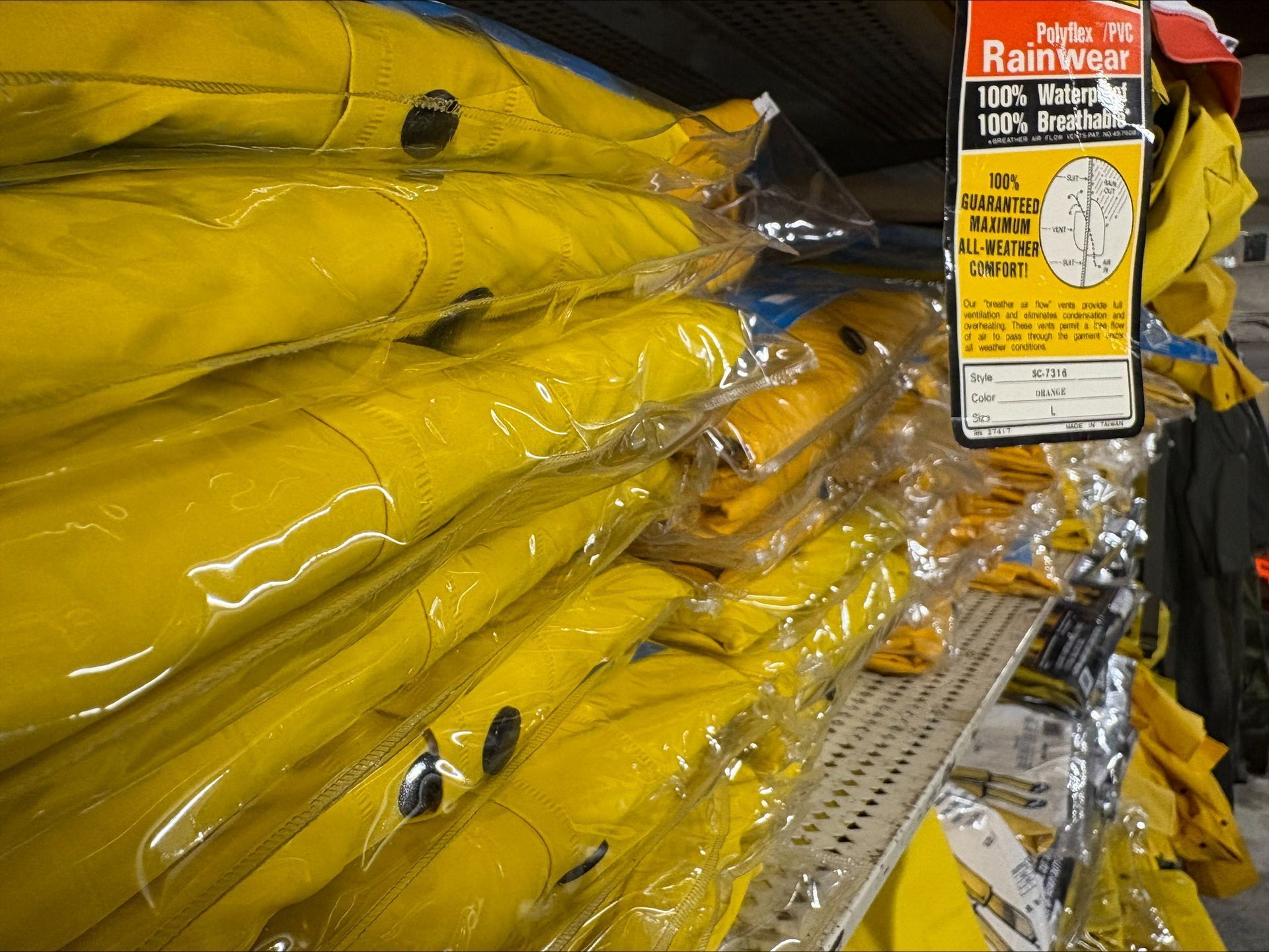 Yellow raincoats stacked on a shelf, in plastic packaging, with a product tag.