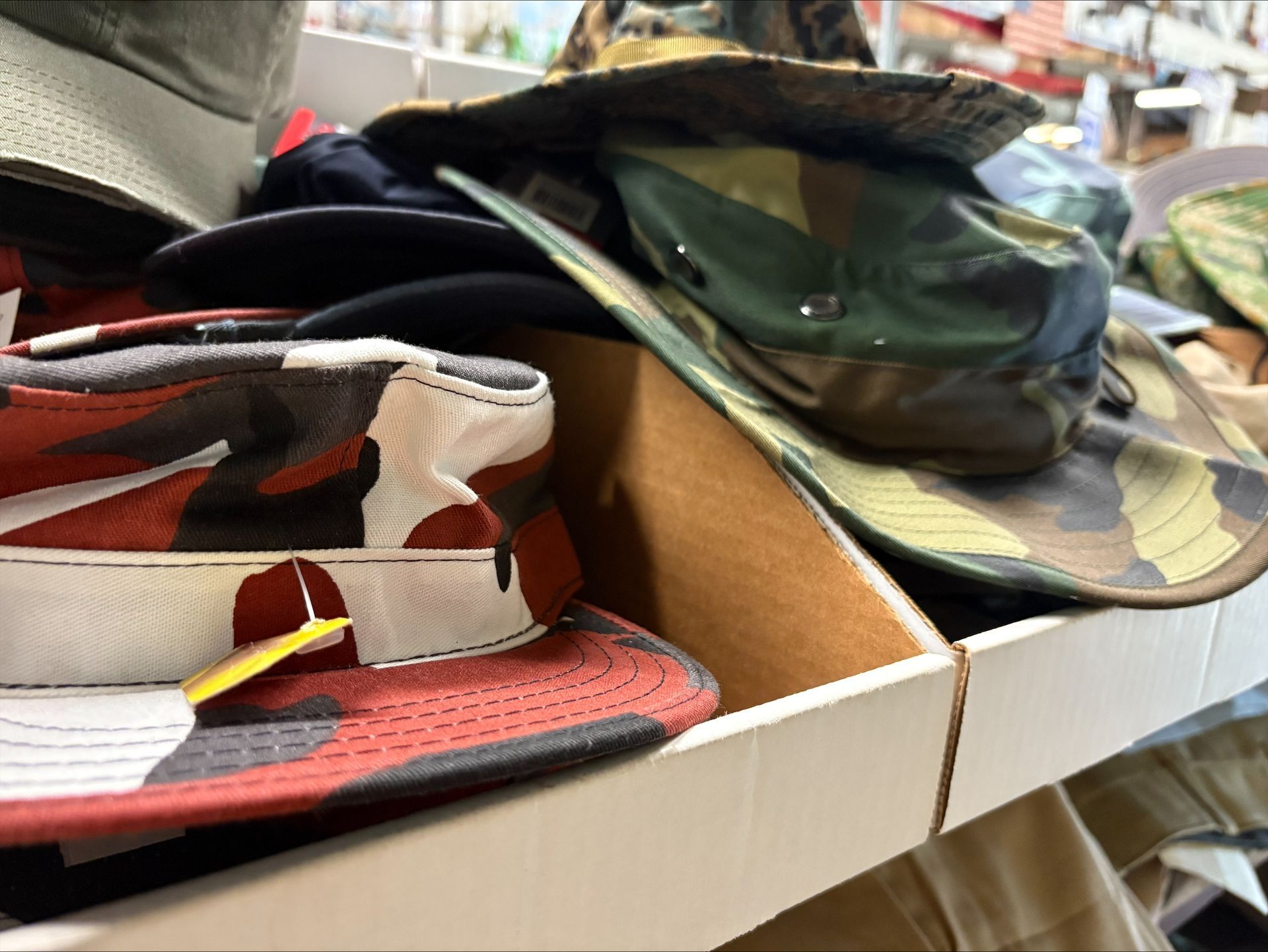 Hats of various colors and camouflage patterns inside a cardboard display case.