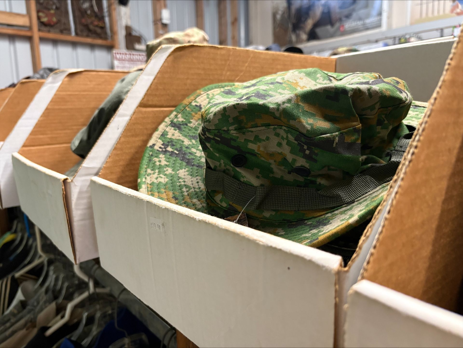 Hats in camouflage patterns inside cardboard bins, possibly for sale in a store.