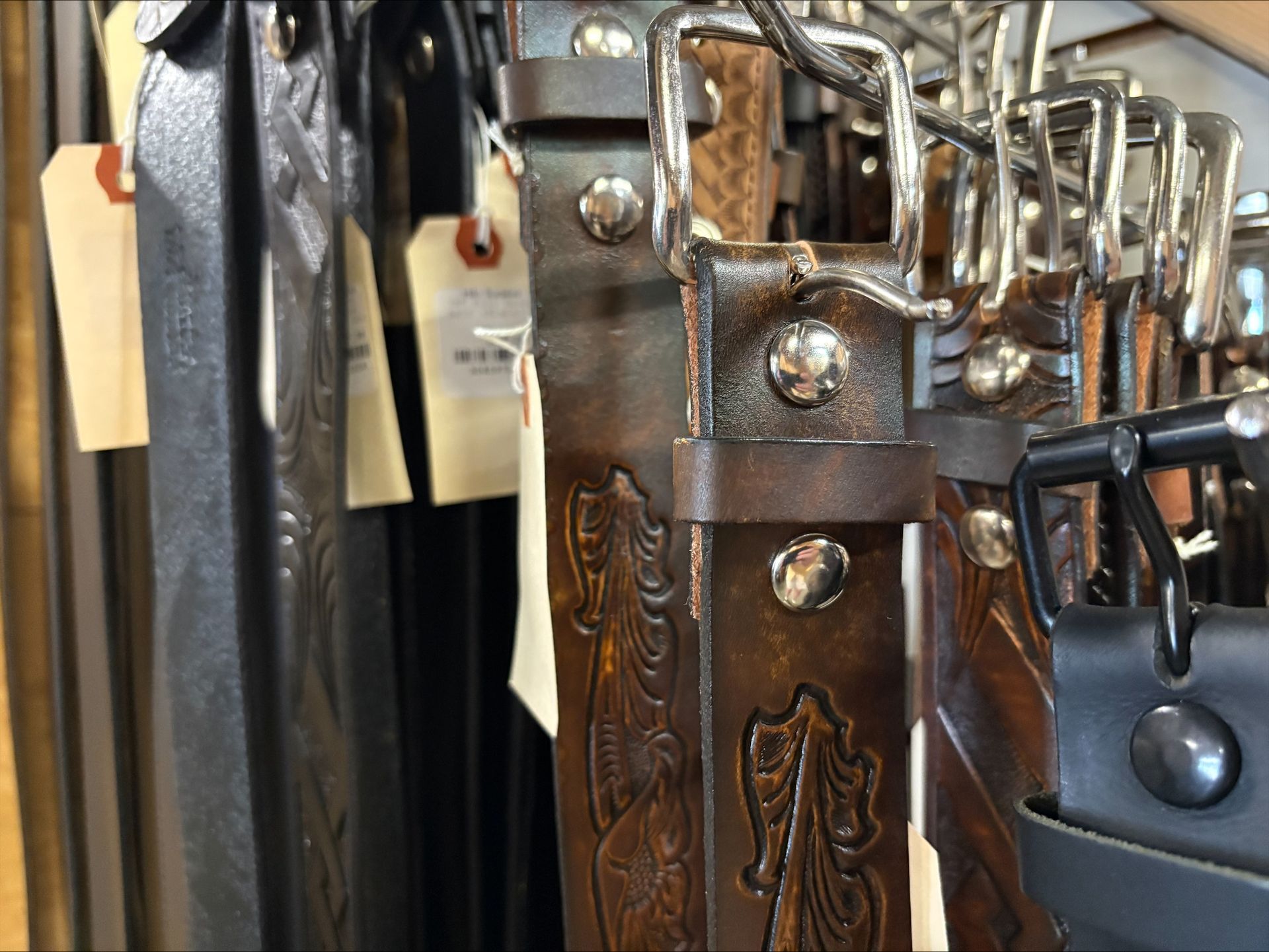 Leather belts with silver buckles and stamped designs on display.