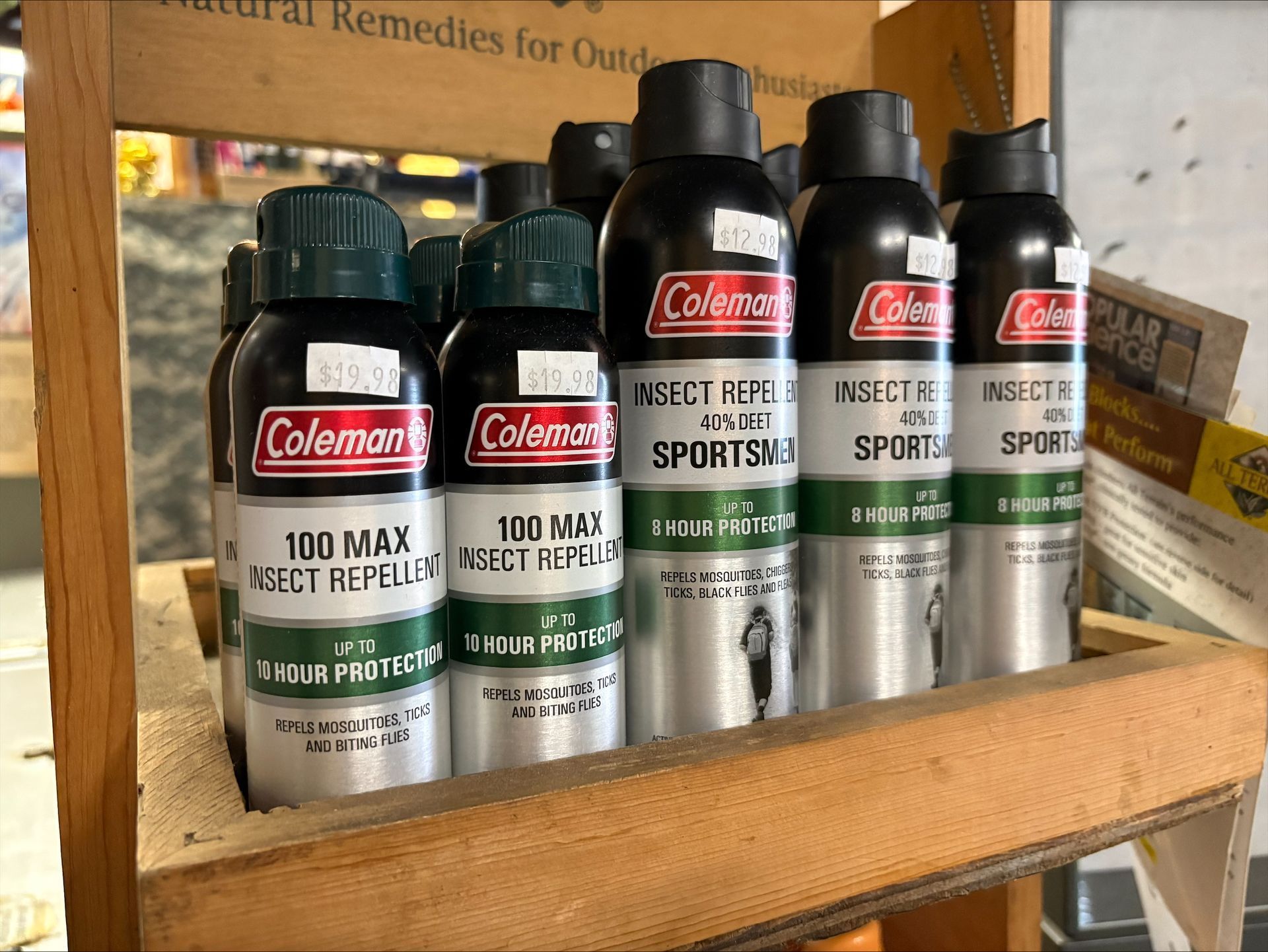Insect repellent spray cans (Coleman brand) in a wooden display shelf.