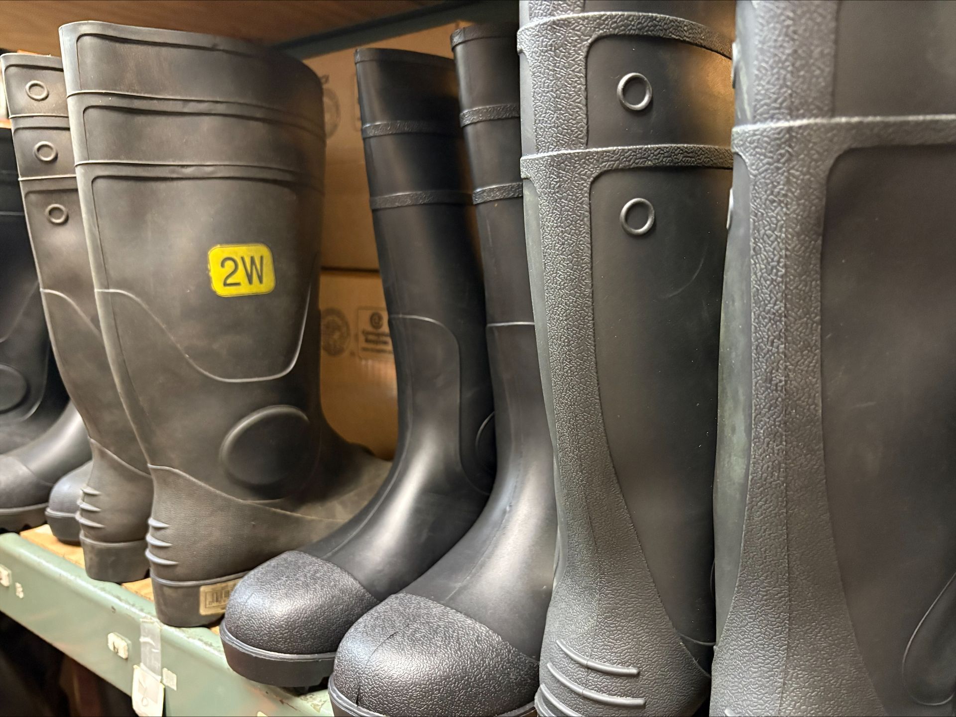 Black rubber work boots on a shelf, various sizes and styles.