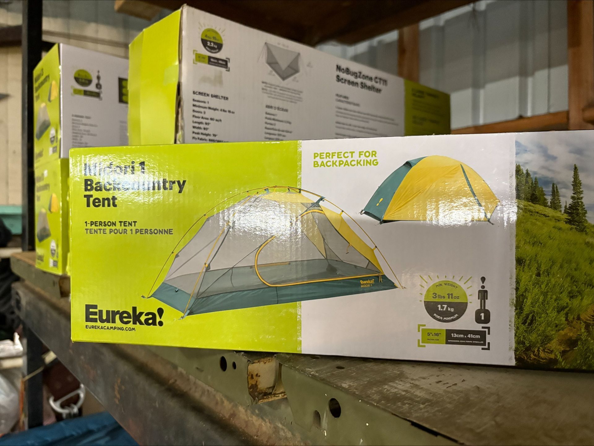 Boxes of Eureka! Backcountry tents on a shelf. The box is yellow and green and features tent illustrations.