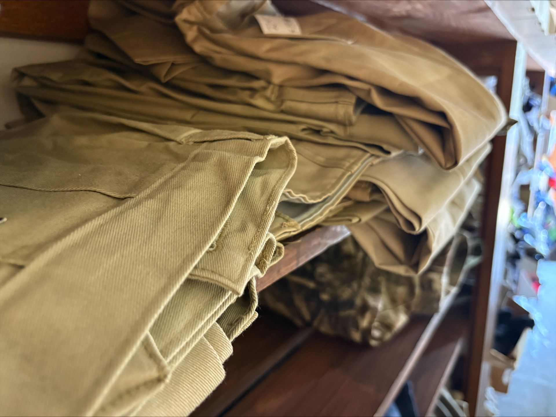 Tan fabric items stacked on a wooden shelf, various folds visible.