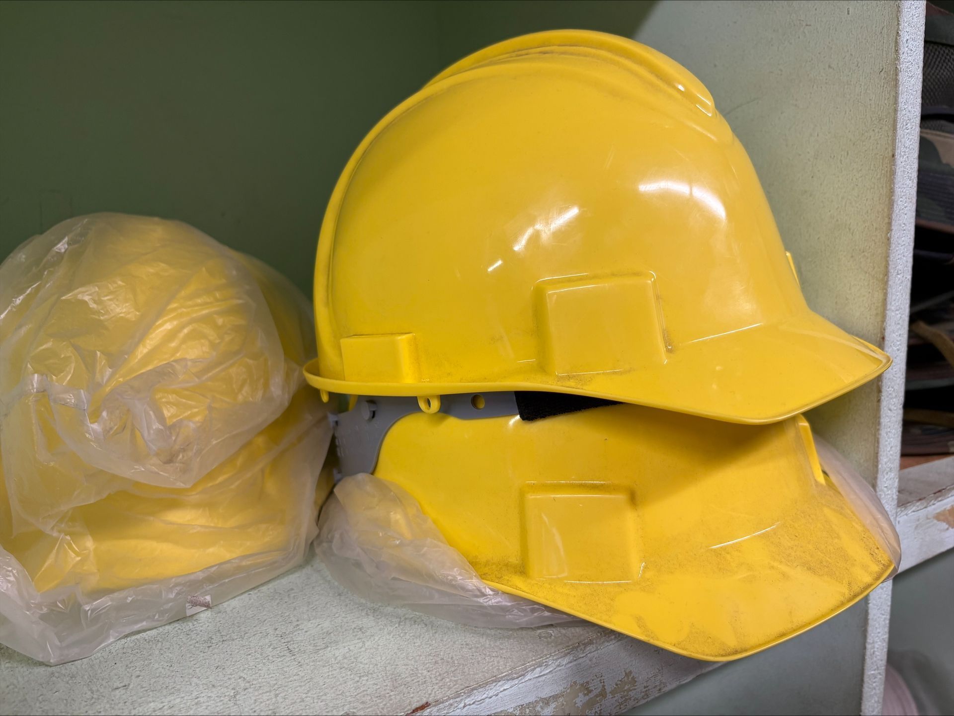 Yellow hard hats, stacked on a shelf; one wrapped in plastic.